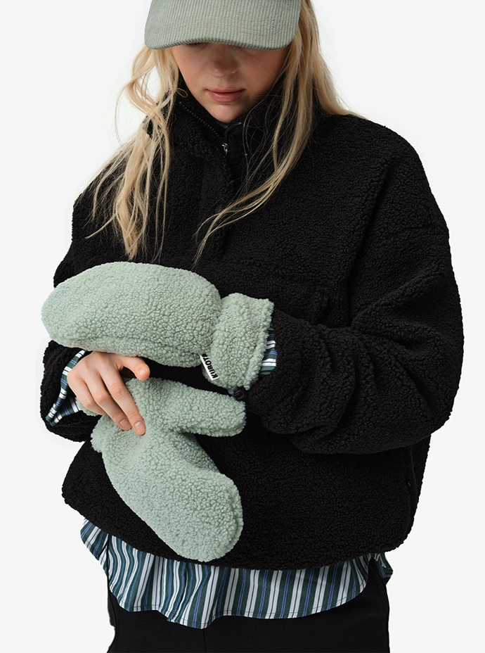 Lookbookowe zdjęcie modelki ubranej w czarną damską bluzę polarową Cushy. W dłoniach trzyma miętowe rękawiczki polarowe Cushy z kolekcji jesień/zima 2025.