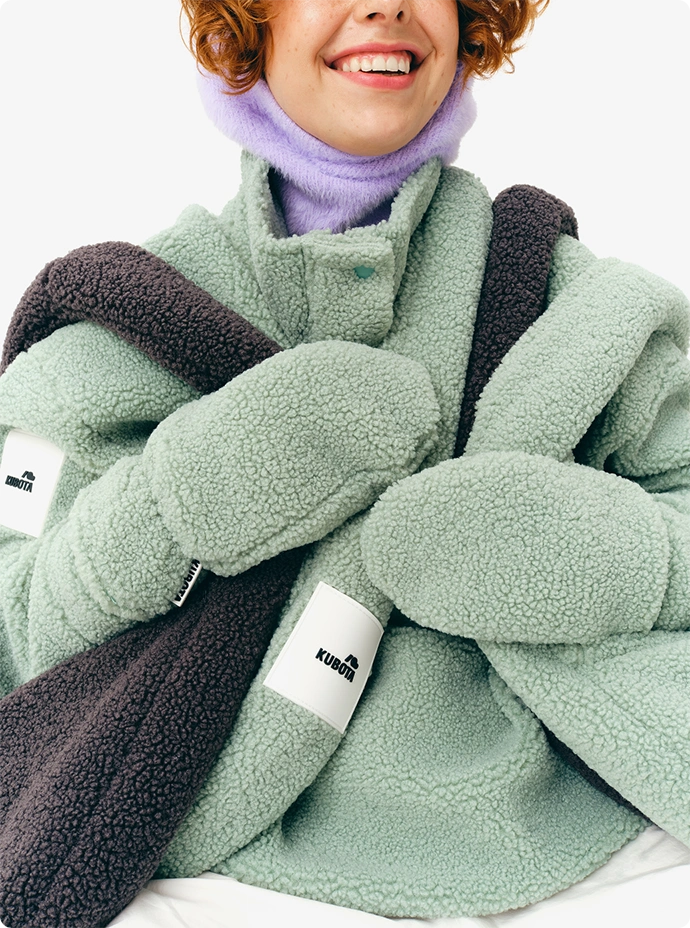 Lookbookowe zbliżenie na uśmiechniętą modelkę ubraną w miętowy polar Kubota. Grafika prezentuje miętowe i grafitowe torby i rękawiczki z kolekcji jesień/zima 2025.