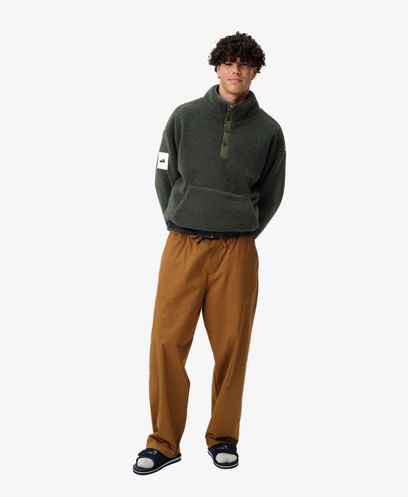 Model prezentuje stylizację lookbookową Kubota. Ubrany jest w ciemnozieloną męską bluzę polarową Cushy oraz ciemnozielone klapki Sztruks z kolekcji jesień/zima 2025.