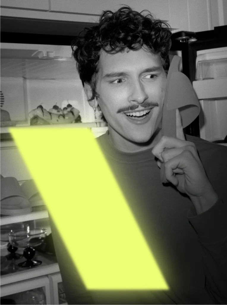 Zdjęcie lookbookowe promujące pomarańczowe klapki Plain 2.0 podczas Black Weeks. Humorystyczna, czarno-biała fotografia z neonowym akcentem, będącym częścią logo Kubota, przedstawiająca modela trzymającego klapek przy uchu jak telefon.