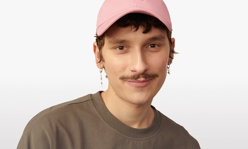 Baner kategorii Mężczyzna. Model noszący różową czapkę z daszkiem od Kuboty.