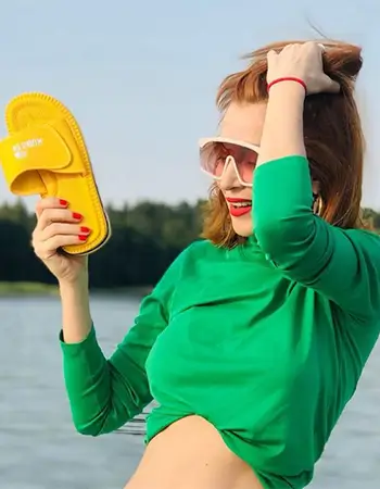 Zdjęcie @adafijal w zielonym topie i białych okularach, pozującej z żółtym klapkiem Kubota Rzep.