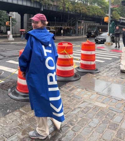 Zdjęcie @joanna_osyda w kobaltowej parce przeciwdeszczowej z dużym, pionowym logo Kubota na plecach na tle miejskiej ulicy.