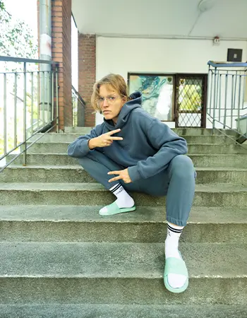 Zdjęcie @kasiagandor kucającej na schodach w szarym dresie, miętowych klapkach Kubota i białych skarpetkach.