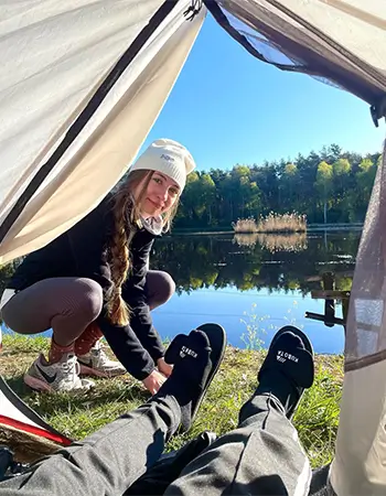 Zdjęcie @matizienba ukazujące perspektywę z wnętrza namiotu na jezioro. Na pierwszym planie czarne klapki Kubota Rzep.