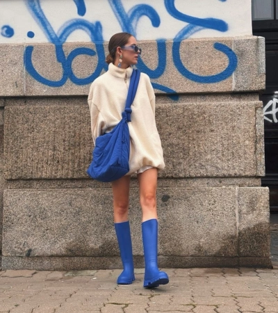 Zdjęcie @matviivka w kremowym polarze i wysokich, niebieskich kaloszach Kubota na tle ściany z graffiti.