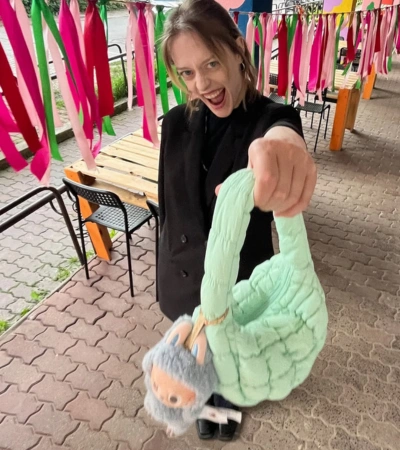 Zdjęcie @pamiszka trzymającej miętową, pikowaną torebkę Kubota z puszystym brelokiem na tle kolorowych wstążek.