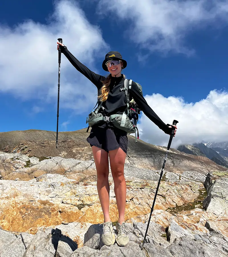 Zdjęcie @sylvvia.m w wysokich górach, trzymającej kije trekkingowe i ubranej w czarny bucket hat Kubota.