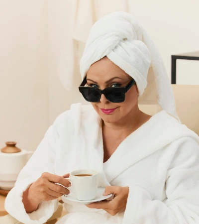 Zdjęcie @trojanowska.official w białym szlafroku i czarnych okularach przeciwsłonecznych od Kuboty z filiżanką kawy.