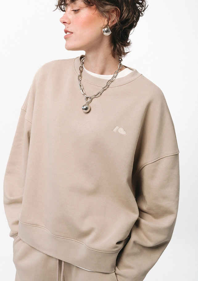 Zdjęcie lookbookowe z kolekcji SS26 prezentujące beżową bluzę oversize Easy. Kadr z bliska skupia się na detalach bawełnianego dresu z dyskretnym, jasnym logo na piersi.