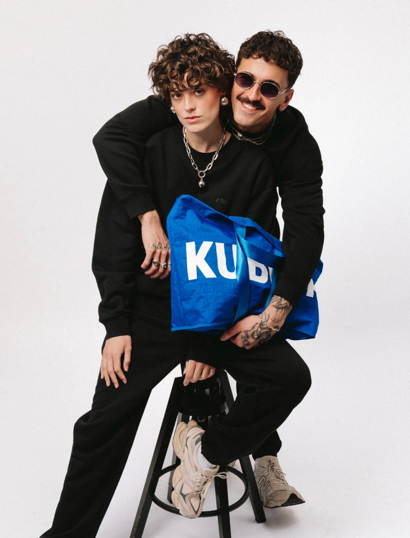 Baner podstrony SS26 Lookbook. Kobieta i mężczyzna w czarnych dresach trzymają dużą, kobaltową torbę shopper.